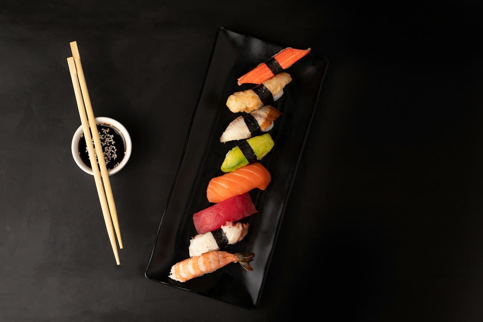 Combinado variado de niguiris em prato preto com shoyu e hashi