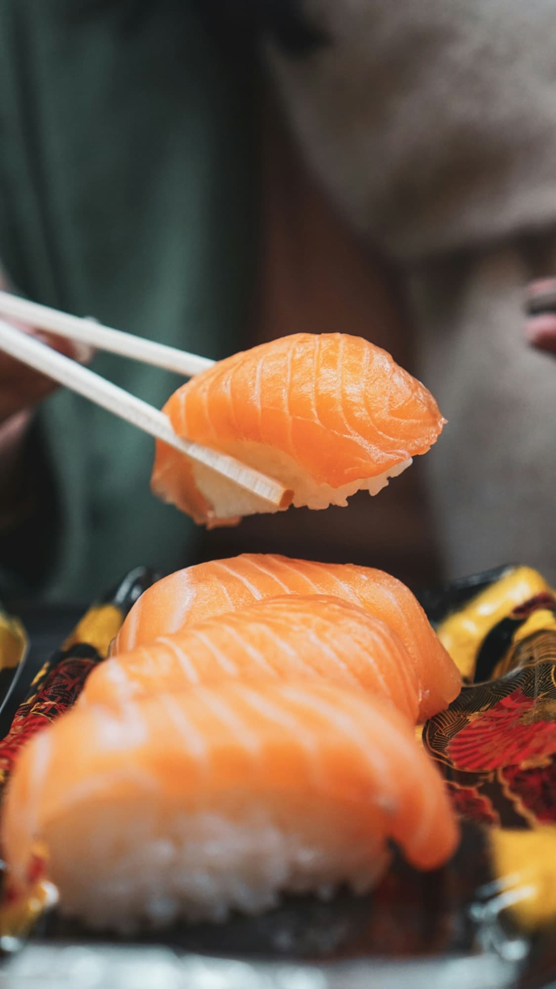 Niguiri de salmão segurado com hashi sobre bandeja de sushi