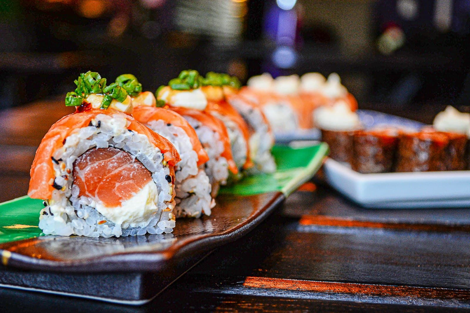 Uramaki de salmão com cebolinha servido em prato escuro